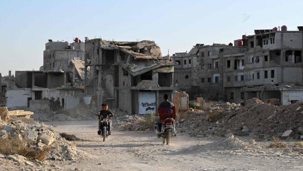 أشخاص يركبون دراجاتهم النارية أمام مبانٍ مدمرة في داريا، على مشارف دمشق (أ ف ب)
