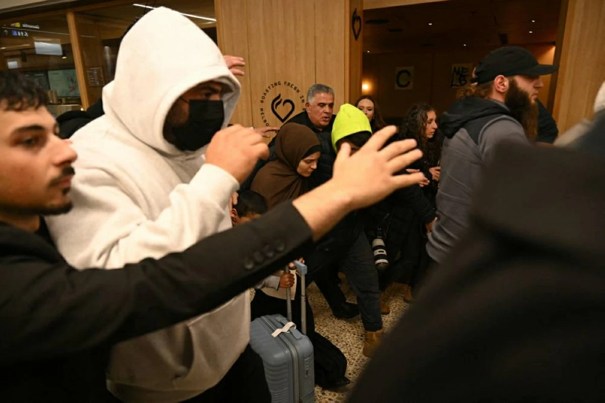 An Australian woman (C) returning from Syrian refugee camps where they have been staying since the Islamic State's demise walks past members of the media as they arrive at the airport in Melbourne on May 7, 2026. A group of women linked to Islamic State jihadists face arrest when they land in Australia on May 7, returning home years after allegedly sneaking into Syria to join the jihadist group's self-declared caliphate. Widely known as the 'ISIS brides', the case has stirred strong feelings in Australia. (Photo by WILLIAM WEST / AFP)