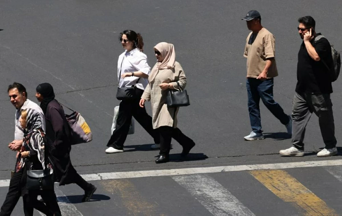 مشاة يعبرون طريقاً على طول ميدان صادقية في طهران (أ ف ب)