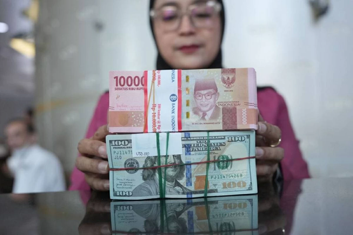 موظفة تحمل رزمتي روبية ودولار في مكتب صرافة بجاكرتا