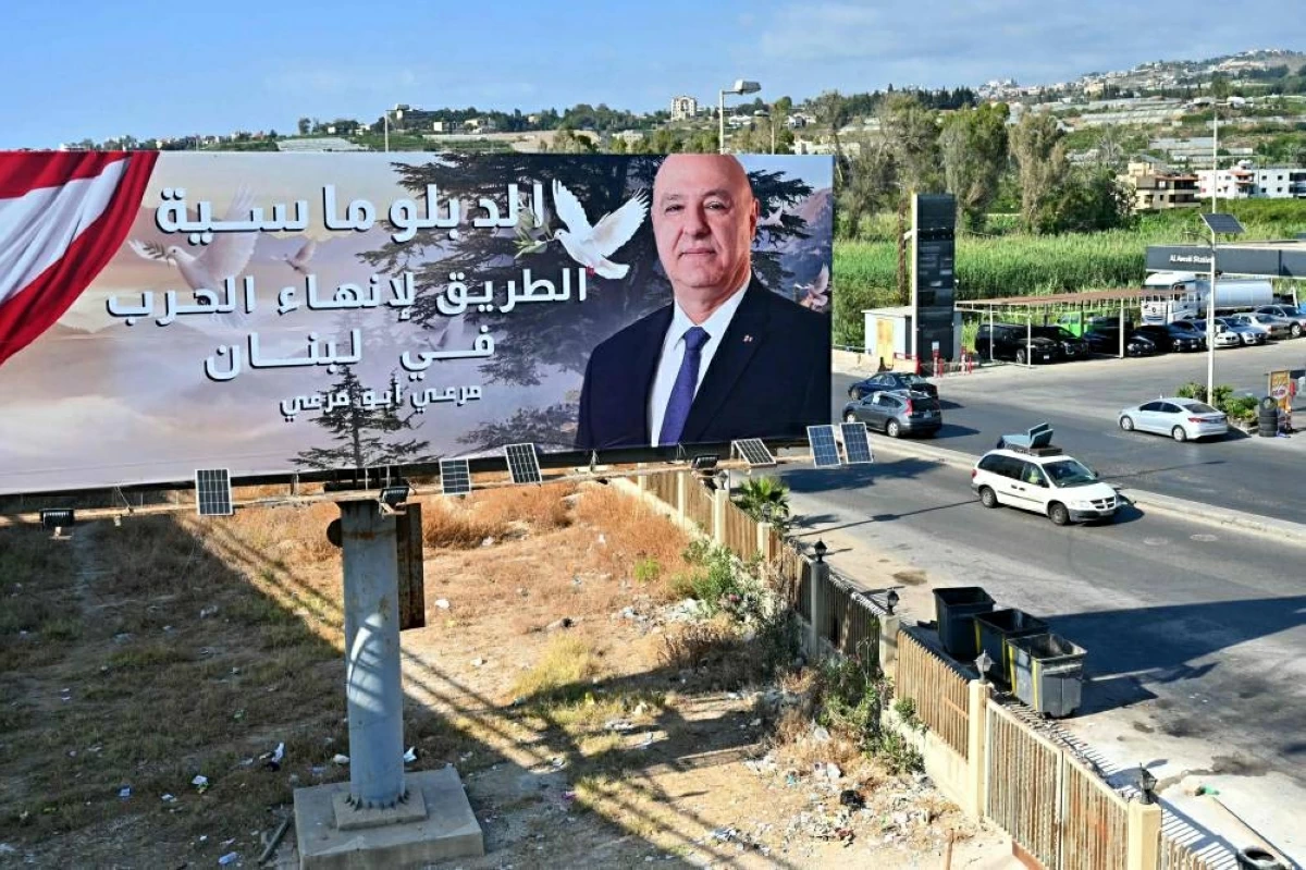 نازحون لبنانيون يعودون إلى قراهم ولوحة إعلانية عليها صورة عون مكتوب عليها «الدبلوماسية هي السبيل لإنهاء الحرب في لبنان» (أ ف ب)