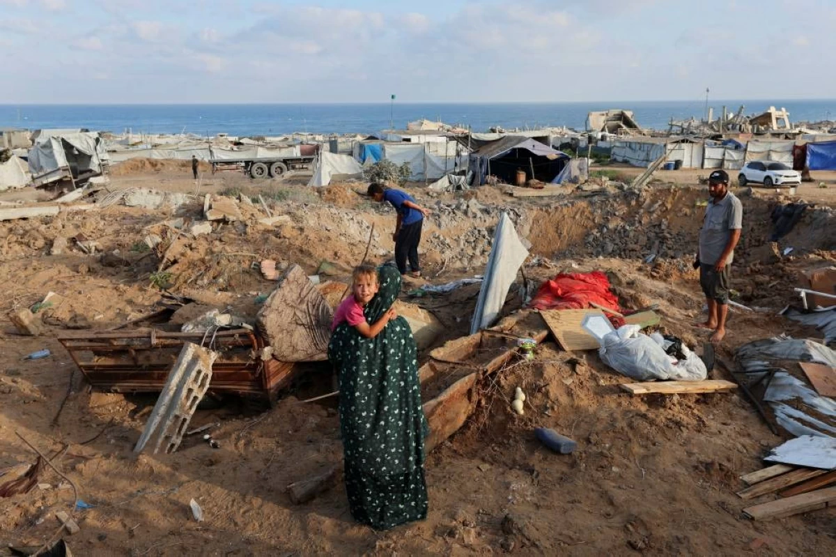 فلسطينيون يتفقدون موقع غارة إسرائيلية استهدفت النازحين في غزة (رويترز)