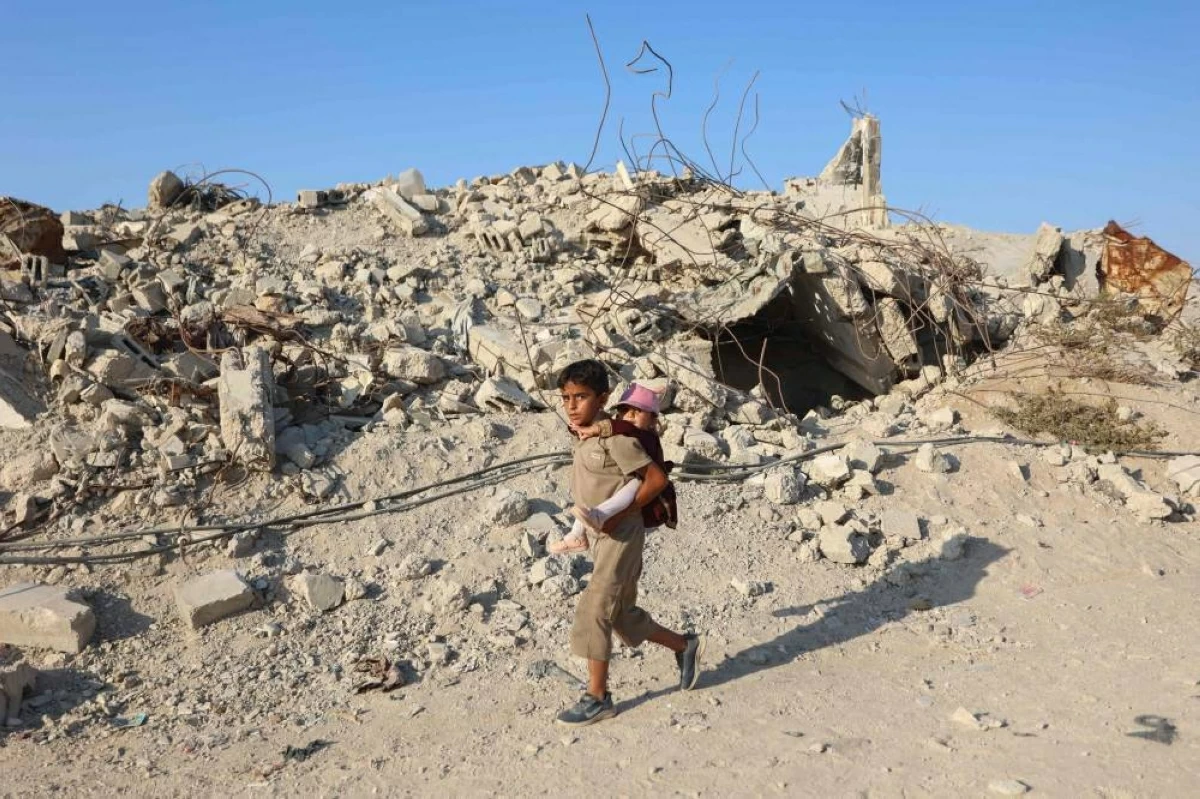 فتى فلسطيني يسير بين الأنقاض حاملا  فتاة صغيرة على ظهره في مخيم جباليا (ا ف ب)