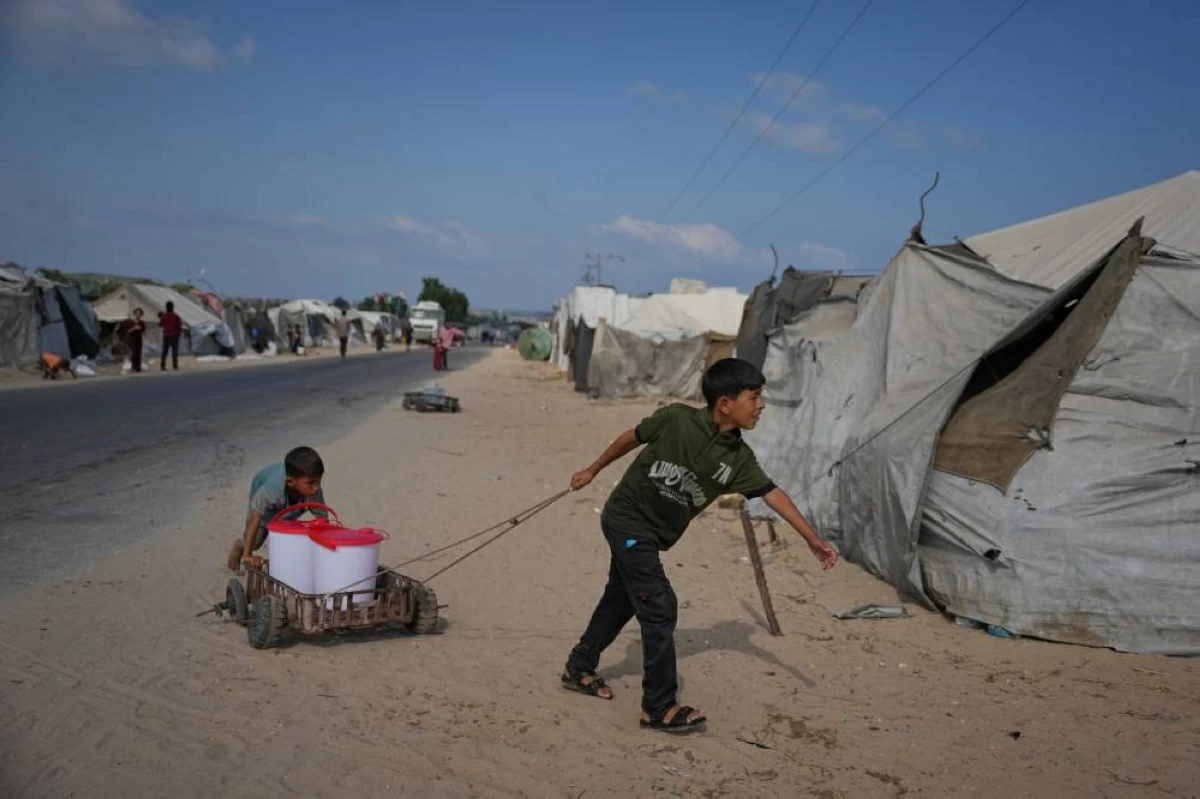 أطفال فلسطينيون يجرون عربة تحمل أوعية مياه في مخيم للنازحين بدير البلح (ا ب)