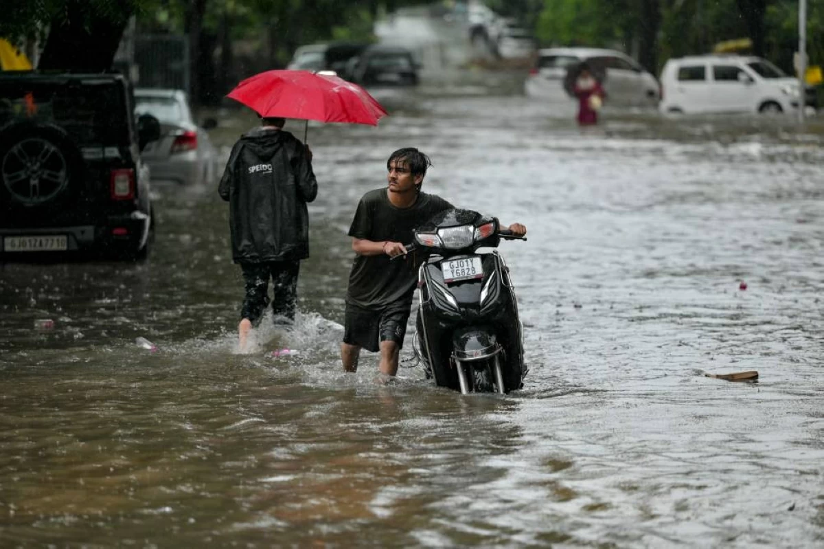 A man pushes his scooter through a water-logged street during rainfall in Ahmedabad on September 14, 2026. (Photo by Shammi MEHRA / AFP)