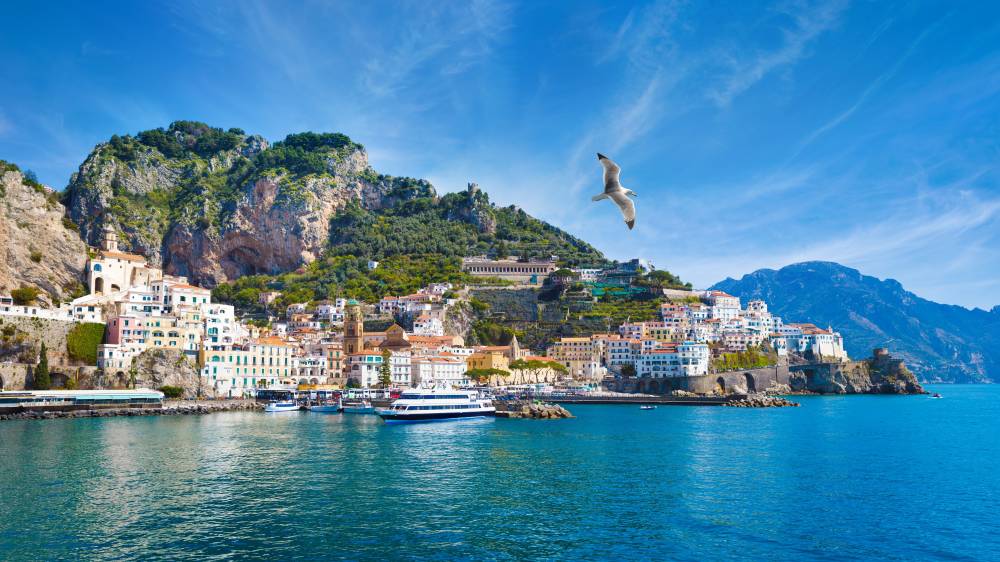 Panoramic view of Amalfi, Italy. Colorful buildings perched on cliffs along serene Mediterranean Sea under clear blue sky. Amalfi coast is most popular travel and holiday destination in Europe