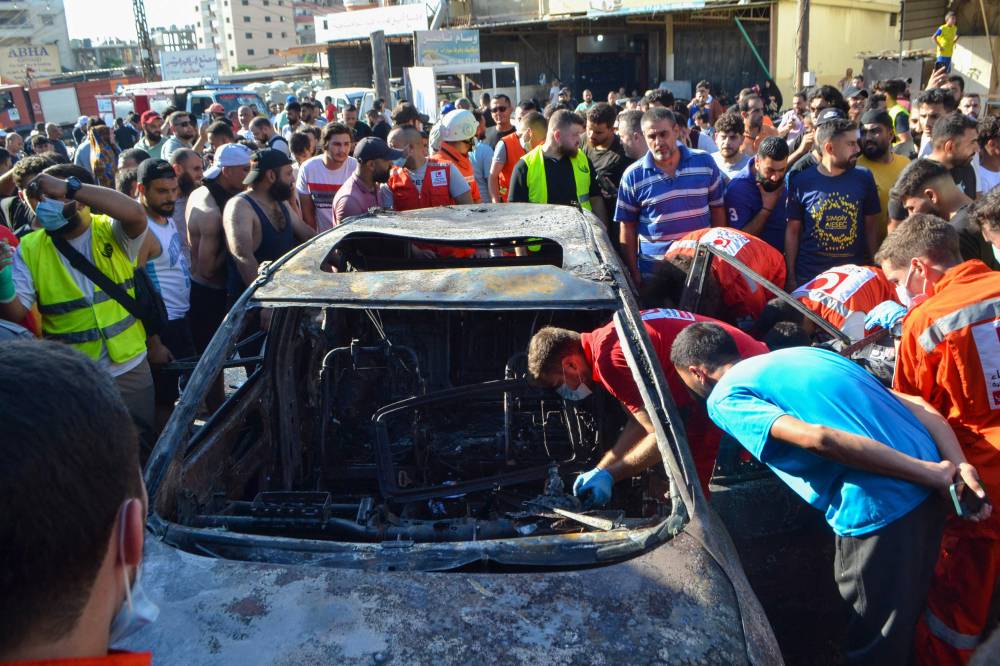 مسعفون يتفقدون سيارة محترقة، استُهدفت في غارة جوية إسرائيلية، في منطقة العيرونية قرب مدينة طرابلس (أ ف ب)