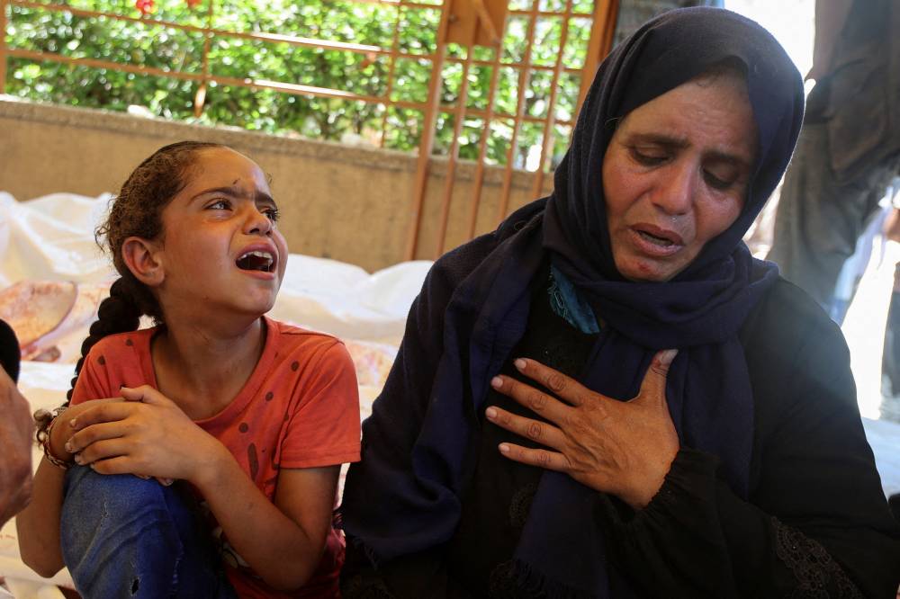 سيدة فلسطينية، مع ابنتها، تبكي ابنها الذي قُتل بنيران إسرائيلية قرب نقطة توزيع مساعدات في رفح (رويترز)