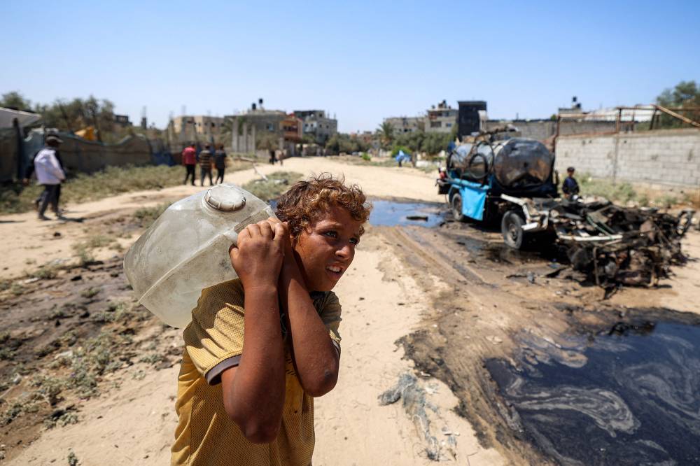 (ا ف ب) طفل فلسطيني يحمل وعاءً مملوءًا بالمياه المأخوذة من خزان متنقل في مخيم النصيرات