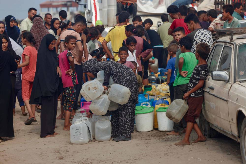 فلسطينيون يصطفون للحصول على مياه الشرب في ظل الحر الشديد في منطقة المواصي (أ ف ب)