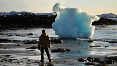 رجل يشاهد كتلة جليدية عائمة على الساحل الغربي في مدينة نوك (أ.ف.ب)