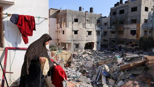 فلسطينية تجمع متعلقات عائلاتها قرب مسكنها الذي دمره القصف (رويترز)
