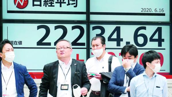 Pedestrians stand in front of an electronic quotation board displaying share prices of the Tokyo Stock Exchange in Tokyo on June 16, 2020. - Tokyo stocks opened sharply higher on June 16 as investors took heart from rallies on Wall Street with eyes shifting onto the Bank of Japan's policy decision later in the day. (Photo by Kazuhiro NOGI / AFP)