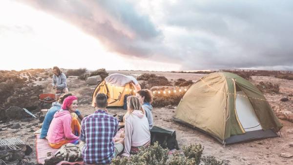 Happy friends making barbecue picnic camping in the desert at sunset - Young people having fun preparing dinner - Travel, tour adventure on nature, vacation and friendship concept