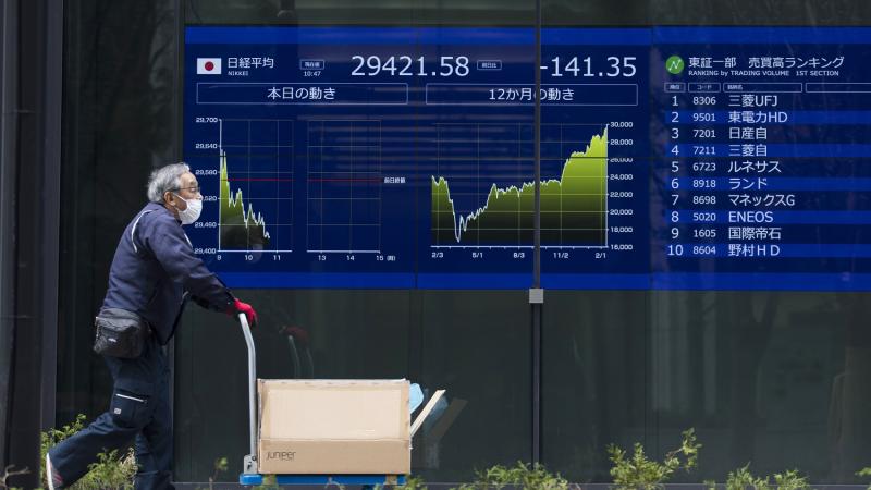 أحد المارة يجر عربة أمام شاشة للأسهم في طوكيو 
