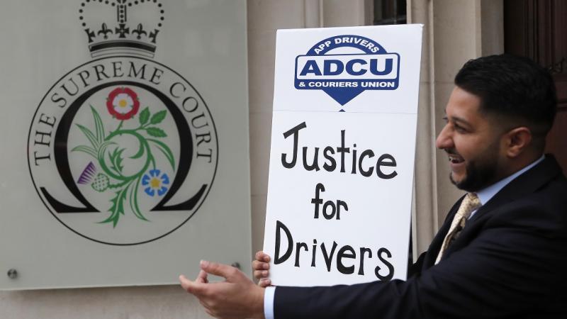 رئيس اتحاد سائقي التطبيقات ياسين إسلام يقف مع ملصق أمام المحكمة العليا