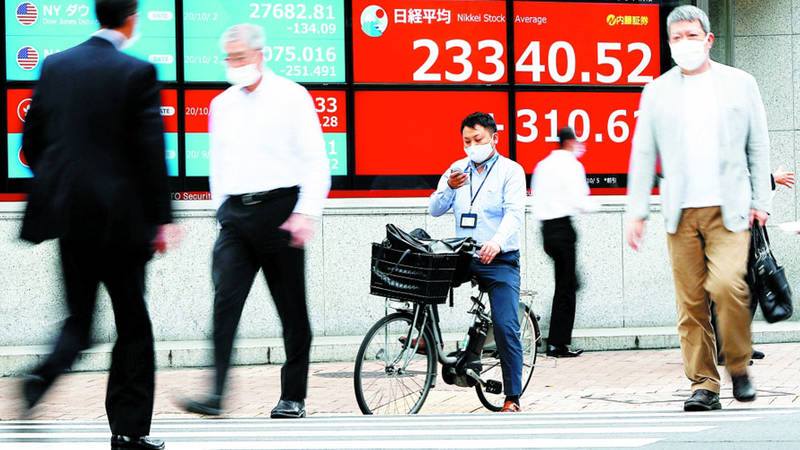 مارة يرتدون أقنعة واقية يمشون أمام شاشة تعرض متوسط سهم نيكاي في طوكيو (رويترز)