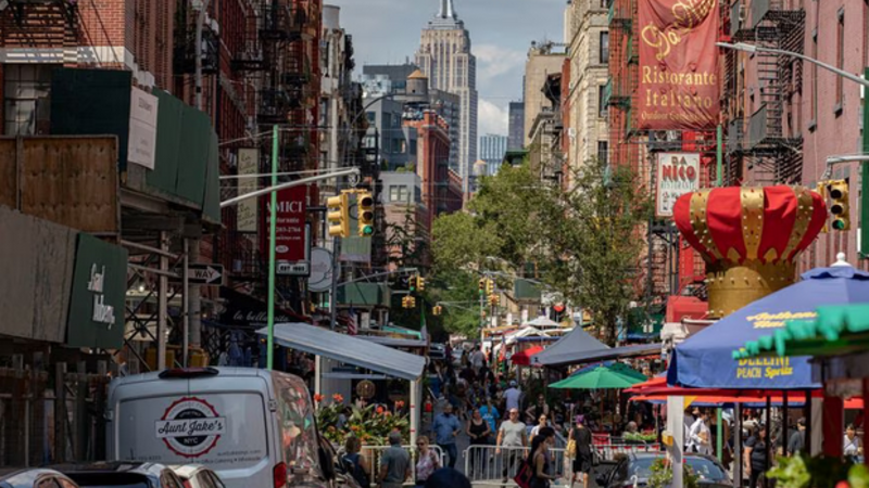 أشخاص يسيرون في شارع تصطف على جانبيه أماكن جلوس خارجية للمطاعم في حي ليتل إيطالي في مانهاتن، نيويورك، الولايات المتحدة (رويترز)