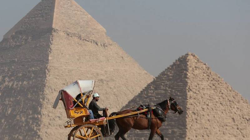 سائحون يركبون عربة يجرها حصان أمام هضبة الأهرامات في الجيزة (رويترز)