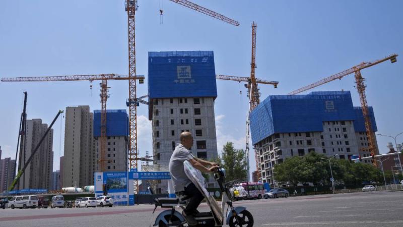 رجل يركب دراجة كهربائية يمر بجوار مبانٍ سكنية قيد الإنشاء في بكين (أ ب)