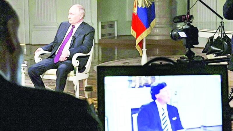  بوتين يتحدث مع الصحفي الأمريكي كارلسون الذي يظهر على شاشة متابعة (أ.ب)