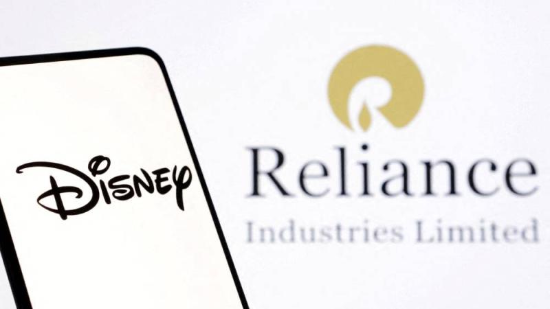 شعار «ديزني»على هاتف ذكي أمام شعار «ريلاينس إندستريز» (رويترز)
