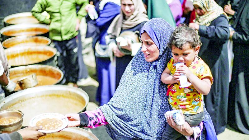 امرأة فلسطينية تحمل طفلاً تحصل على حصتها من وجبة ساخنة في نقطة توزيع طعام بمخيم النصيرات