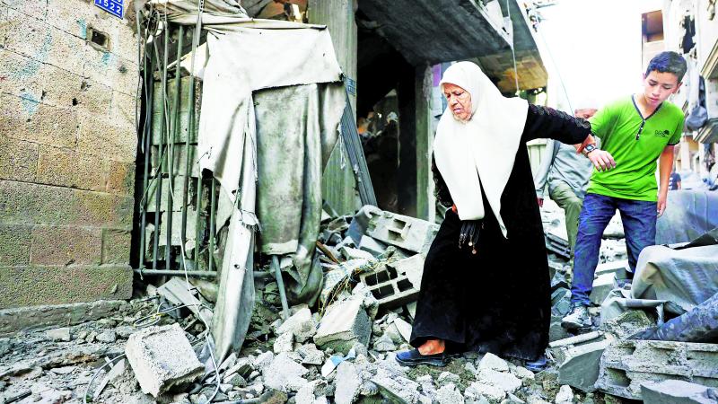 فتى يساعد امرأة مسنة أثناء سيرها وسط الأنقاض بعد غارات إسرائيلية على جباليا 