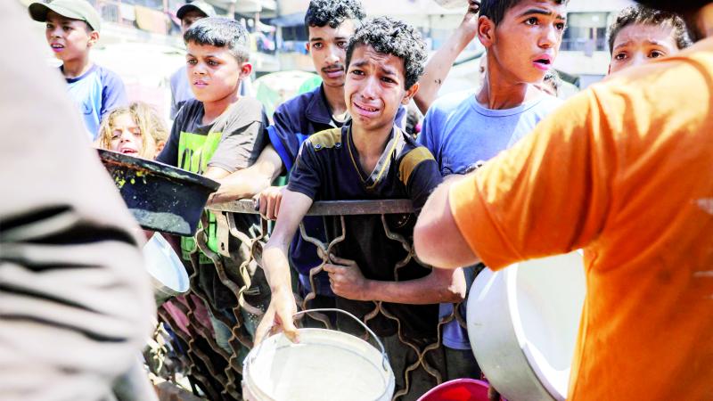أطفال يصطفون مع أوانٍ لتلقي وجبات الطعام من مطبخ خيري في مدينة غزة 