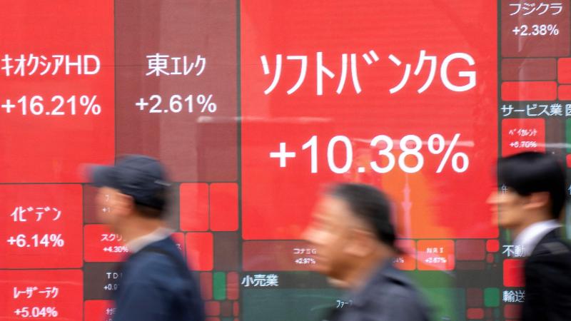 مارة أمام لوحة تعرض تحركات الأسهم المدرجة في بورصة طوكيو بما فيها سوفت بنك (أ.ف.ب)