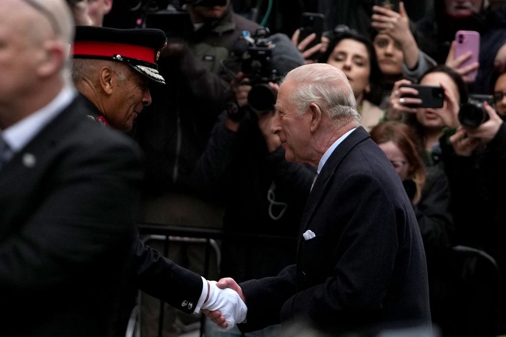 الملك تشارلز يصافح أحد الضباط لدى وصوله إلى أسبوع الأزياء في لندن