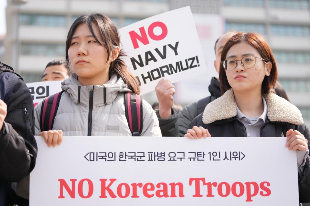 متظاهرتان ترفعان لافتة احتجاج رفضاً لإرسال جنود إلى مضيق هرمز (أ.ب)