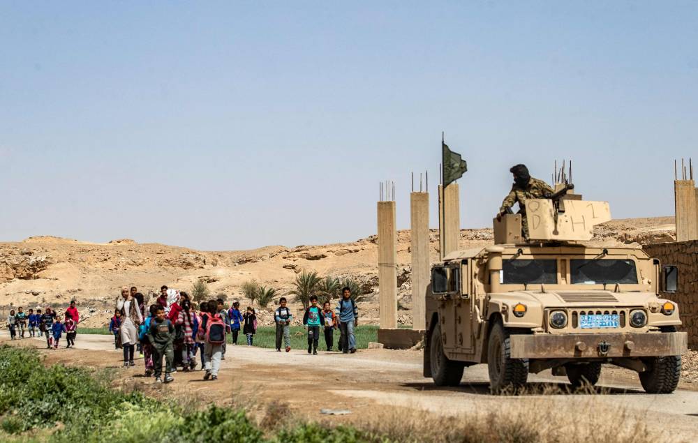 Fighters of the Kurdish-led Syrian Democratic Forces (SDF) stand guard as students return home from school in the village of Baghouz in Syria's northern Deir Ezzor province, on March 24, 2021, where two years ago, the Islamic State Group (IS) made their last stand before being defeated. - In March 2019, after Kurdish fighters and the US-led coalition declared the IS proto-state defeated, Baghouz looked like a churned up wasteland, its roads were dotted with destroyed homes.
Now, residents have started to renovate battered buildings. Children have also returned to school and a handful of businesses have reopened.
But twisted metal wreckage continues to litter the floor, several homes remain abandoned and IS insignia can still be spotted on walls across the village. (Photo by Delil SOULEIMAN / AFP)