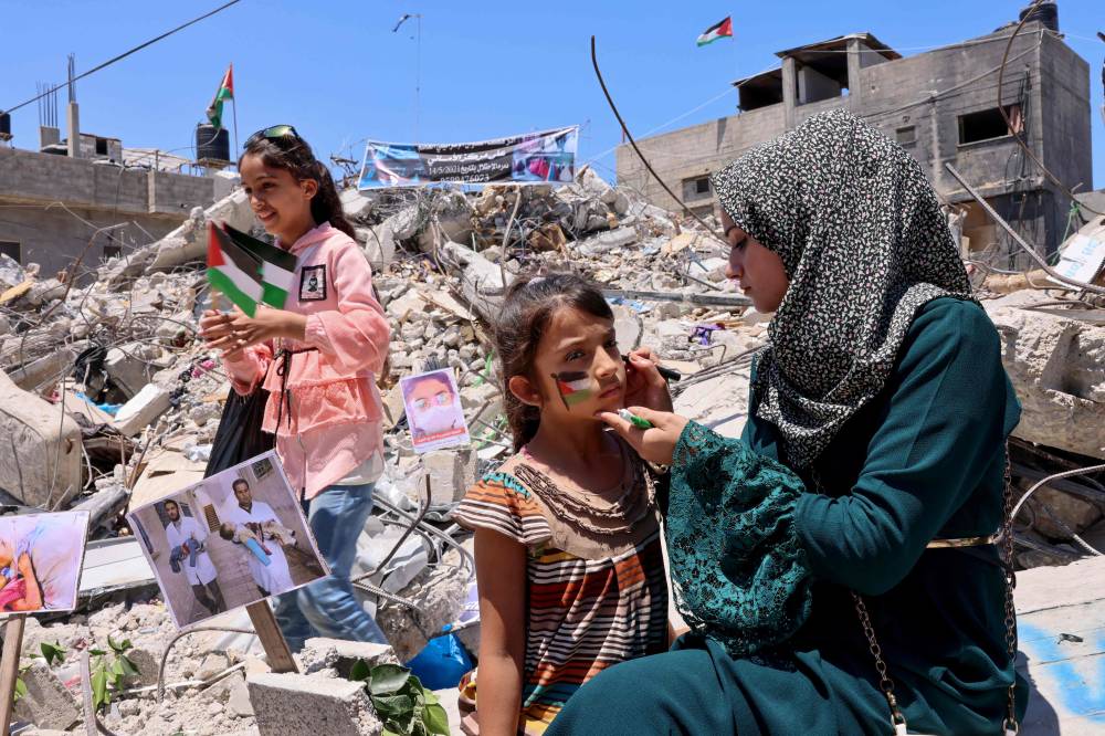 امرأة ترسم العلم الفلسطيني على وجه طفل وسط أنقاض مبان دمرها القصف الإسرائيلي الشهر الماضي في غزة (أ ف ب)