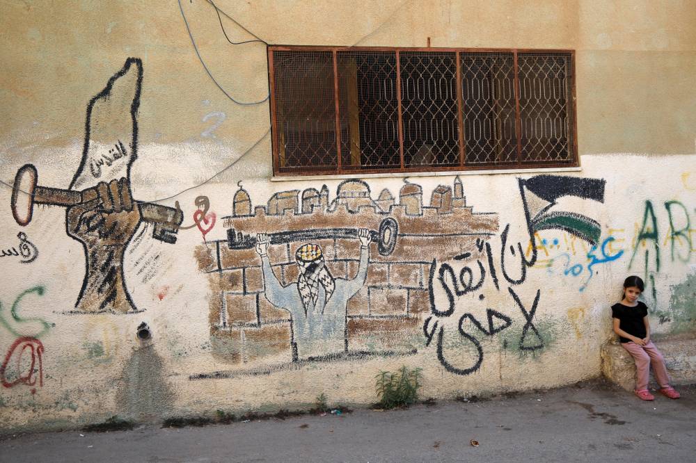 طفلة تجلس بجانب رسم جداري مكتوب عليه «لن أبقى لاجىء» في مخيم الفارعة بالضفة (ا ف ب) 