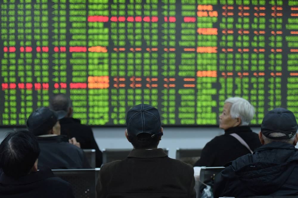متداولون يجلسون أمام لوحة تعرض معلومات الأسهم في إحدى شركات الوساطة في هانغتشو بمقاطعة تشجيانغ، الصين (رويترز) 