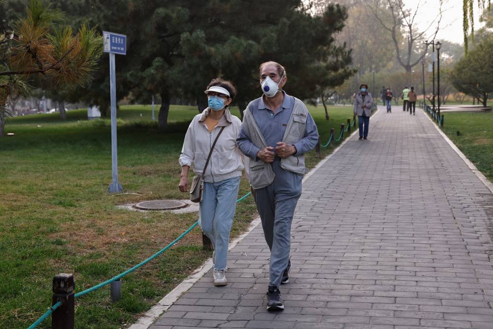 People wearing face masks walk in a park as Beijing issues orange alert for heavy air pollution, in Beijing, China October 31, 2023. REUTERS/Tingshu Wang