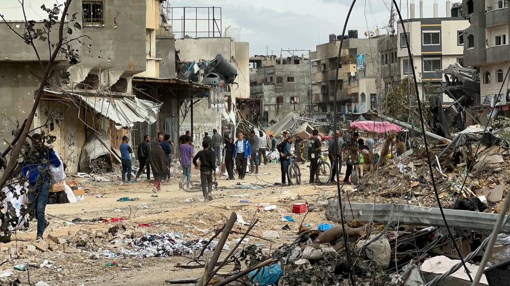 فلسطينيون يسيرون أمام منازل تضررت من الضربات الإسرائيلية خلال الصراع
(رويترز)