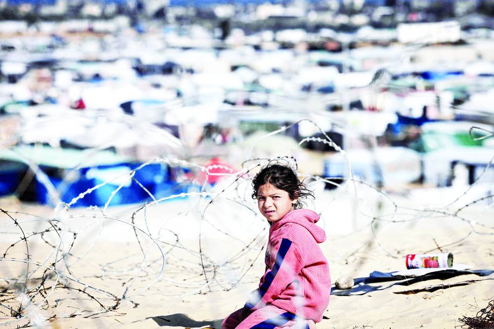 طفلة فلسطينية نازحة تجلس خلف الأسلاك الشائكة في مخيم غرب رفح (أ ف ب)  
