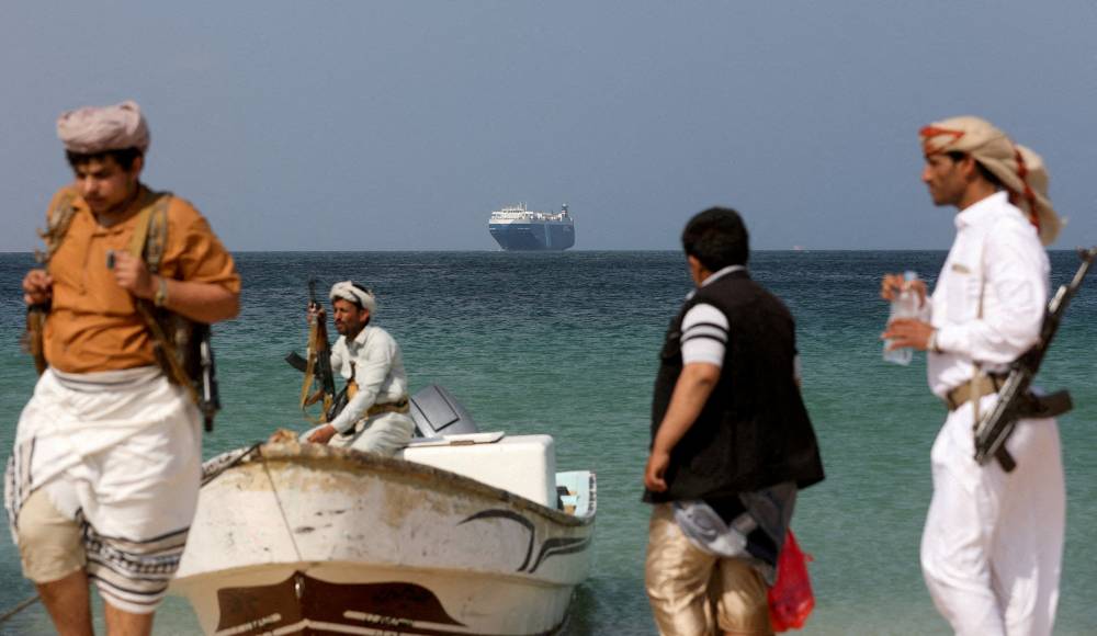 عناصر حوثية مسلحة على شاطئ الصليف، حيث تبدو السفينة التجارية جالاكسي ليدر المختطفة الشهر نهاية العام الماضي (رويترز)