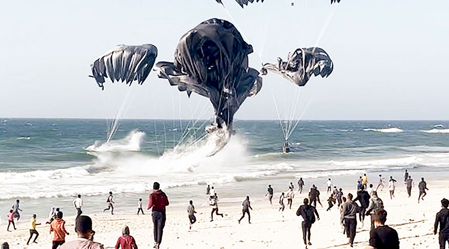 أشخاص يركضون للحصول على مساعدات أسقطتها طائرات أمريكية على غزة (أ ف ب)