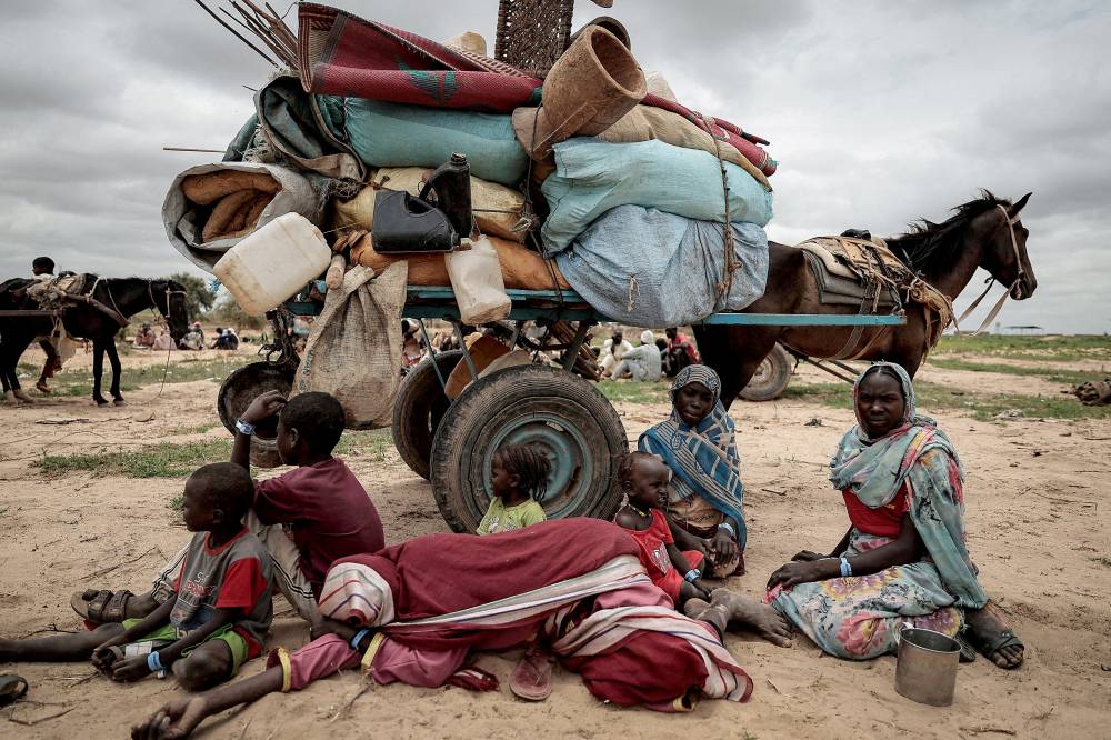 عائلة سودانية فرت من الصراع في دارفور تجلس عند نقطة عبور على الحدود بين السودان وتشاد (رويترز)