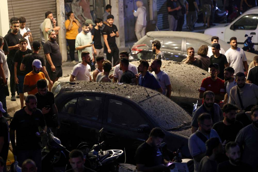 أشخاص يتفقدون السيارات المتضررة في الضاحية الجنوبية لبيروت (أ ف ب)