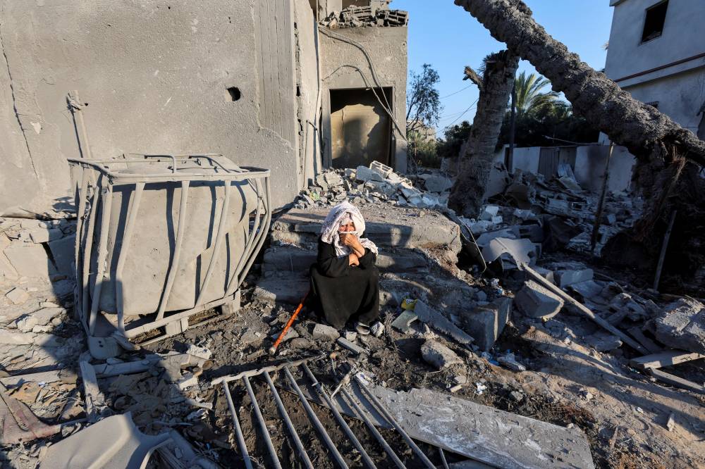 فلسطينية تجلس في موقع غارة إسرائيلية على دير البلح (رويترز)
