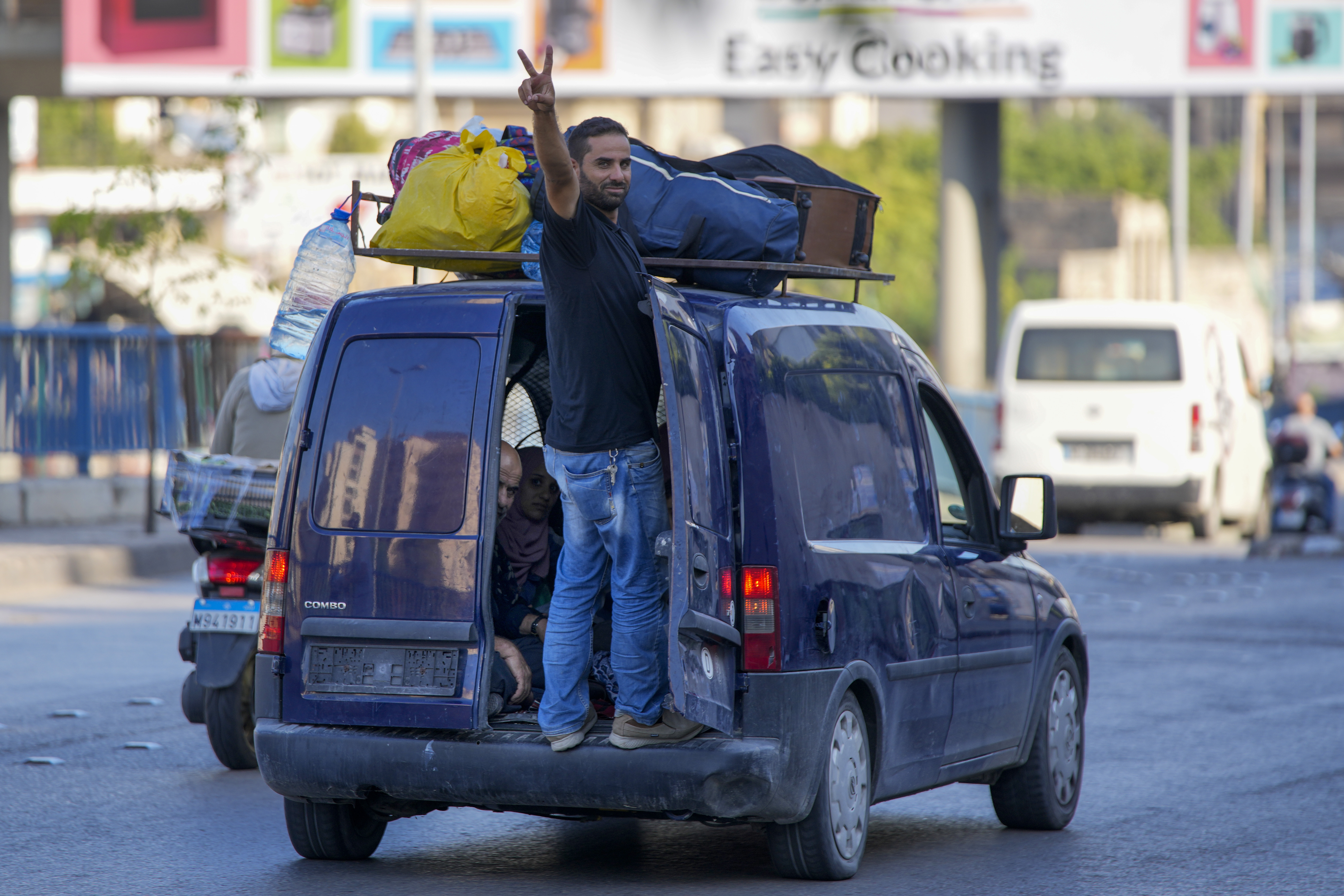 A resident who fled from the southern villages amid ongoing Israeli airstrikes Monday, flashes a victory sign as they drive with their belongings on the top of their car in Beirut, Tuesday, Sept. 24, 2024. (AP Photo/Hassan Ammar)