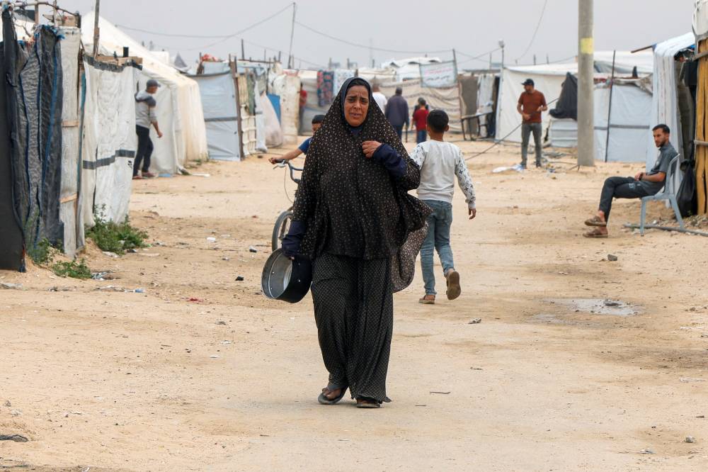  امرأة فلسطينية نازحة تحمل وعاء للطهي في مخيم في خان يونس   (رويترز) 