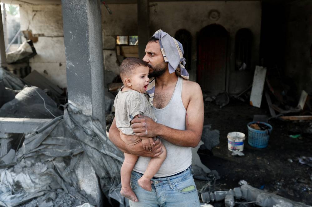    (رويترز) فلسطيني يحمل طفلاً في موقع غارة إسرائيلية على منزل في الزوايدة في وسط القطاع    