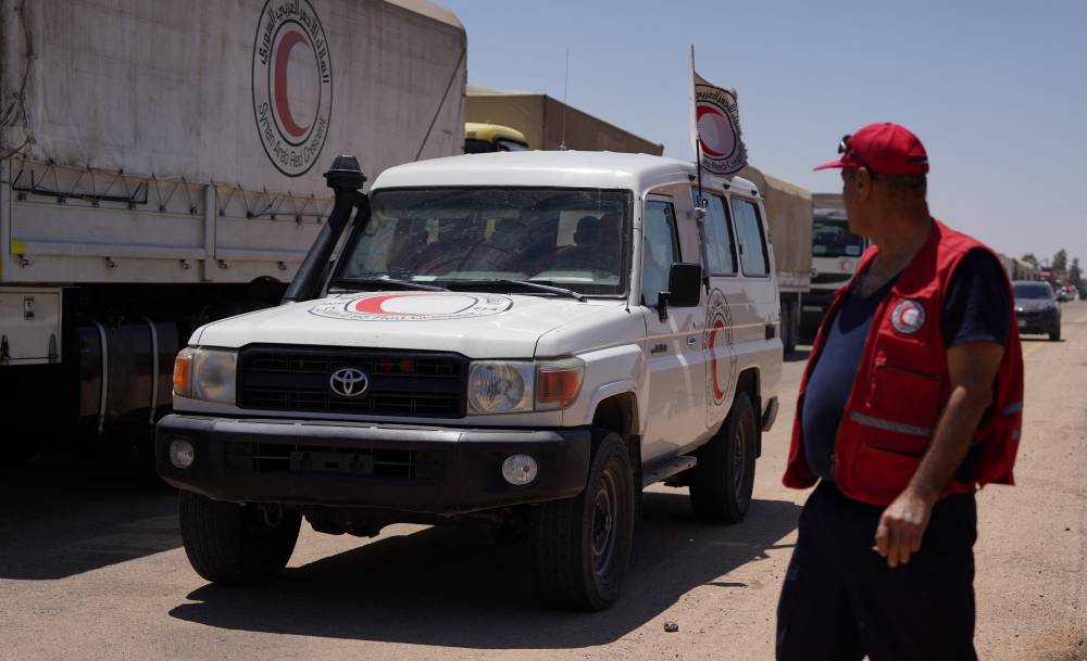  أحد العاملين في الهلال الأحمر السوري يقف بالقرب من مركبة تحمل مساعدات أثناء توجههم إلى السويداء (رويترز)