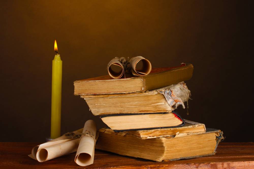 Pile of old books with candle and scroll on brown