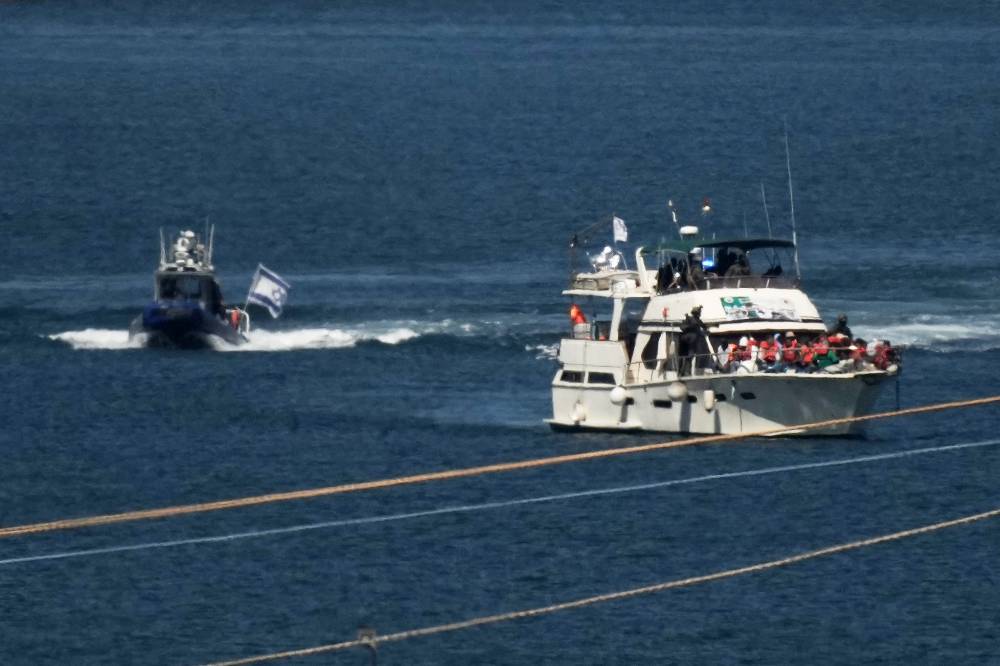 Activists in orange life jackets sit aboard a Gaza-bound Sumud flotilla boat as Israeli navy soldiers sail it into the port of Ashdod, Israel, Thursday, Oct. 2, 2025, after it was intercepted while approaching the Gaza coast. (AP Photo/Leo Correa)